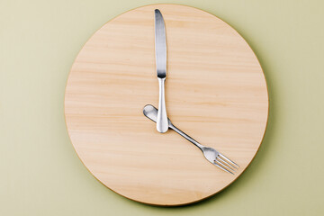 The concept of intermittent fasting and skipping meals. Wooden round tray with cutlery in the form of clock hands