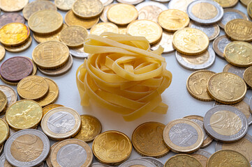Noodles with coins around, on white surface. Rising price of pasta and shortage of wheat. 
