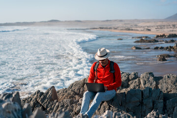 digital nomad sitting on the beach with laptop alone working at sunset.