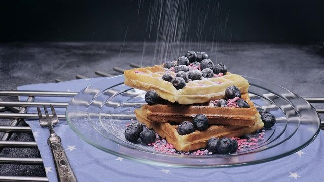 weiche, zarte belgische Waffeln mit frischen Blaubeeren und Schokoladensauce, bestreut mit s&uuml;ssem Puderzucker auf einem Glasteller