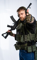 the airsoft player puts his rifle on his shoulder and aims at us with his fingers. a man in an outfit, in headphones, a bulletproof vest, with a backpack on a white background.
