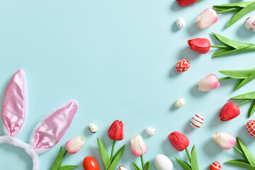 Background with red tulips and painted Easter eggs and rabbit ears on a blue background.