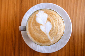 A top down birds eye view of a golden flat white coffee on white plate and textured wooden table in local cafe
