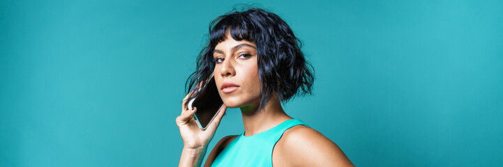 woman talking on her mobile phone – phone talk communication concept -  young people calling cell telephone -  young people talking on the smartphone – studio shot on blue background - horizontal web 