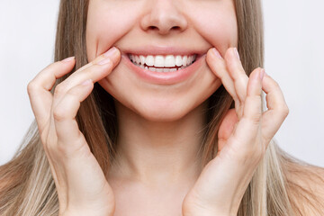 Young caucasian blonde woman demonstrating the beautiful smile with her hands isolated on a white background. Teeth whitening. Oral hygiene, dental health care, perfect even teeth. Dentistry