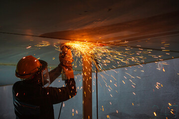 Male worker using electric wheel spark grinding on welder metal carbon steel part roof plate inside...