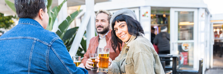 Group of happy friends drinking and toasting beer at brewery bar - Friendship concept with young people having fun together at pub - Focus on middle pint glass - horizontal banner or header