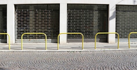 Closed shop with the folding security gates down. Sidewalk, yellow pedestrian barrier and porhyry road in front. Background for copy space