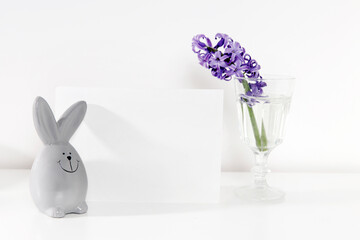 Mock up white frame with modern ceramic easter bunny decor with card on a shelf. White color scheme. Landscape frame orientation.