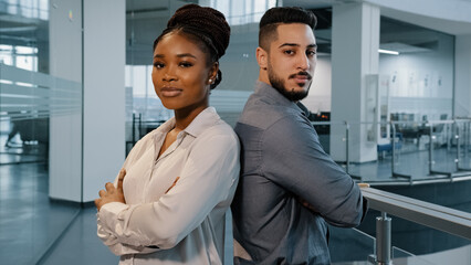 Two confident workers multiracial diverse business co-workers colleagues partners indian arab man and african woman lawyers businesspeople standing in office crossing arms posing looking at camera