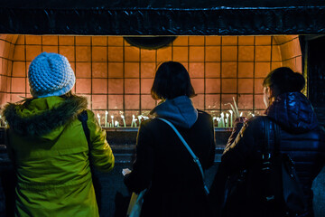 three woman from back burning candles in saint antuan church in istanbul turkey, orange colour, praying and worshipping