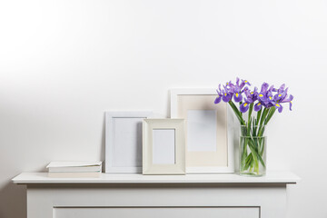 Bouquets of irises in a vase, photo frames on a chest of drawers