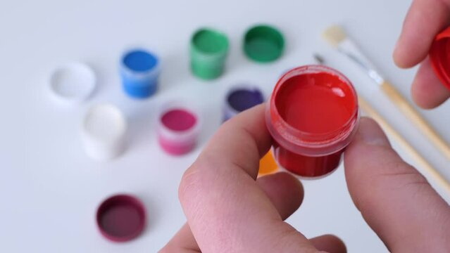Set gouache paints in bright color jars close-up. A set of multicolored gouache on plastic jars. Hobby of creative drawing. Close-up of red paint with refocus on all colors.
