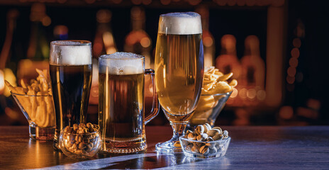 Glass of beer on bar counter. Jugs, mugs, pints of brew beverage, ale, cider on wooden table in...