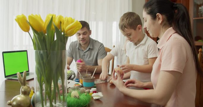 the family sticks stickers on the eggs. on the table is a computer with a green screen