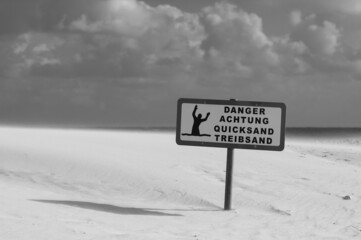 Grayscale shot of the warning sign about quicksand on the beach on a sunny day