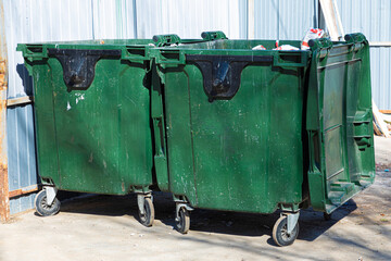 Bright, vivid and colorful urban outdoor background of two green plastic garbage containers or trashcans on garbage collector in sunny spring or summer weather