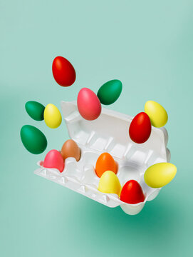 Multicolored eggs flying out from egg container against pastel green background. Creative Easter holiday or food concept. Traditional festive greeting card with empty copy space for text.