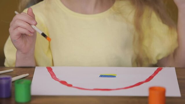 Little girl draws a rainbow and the Ukrainian flag
