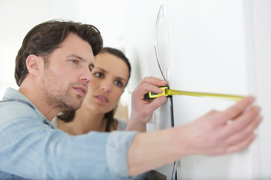 Couple Measuring A Wall With Tape Meter