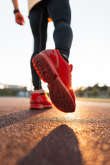 Fashionable sporty man with stylish sportswear in red sneakers walks at sunset, close-up. Guy...
