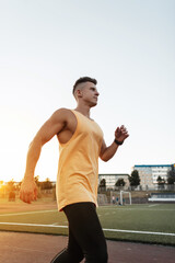 Fototapeta na wymiar Handsome young sporty man athlete in sportswear running outdoors at sunset. Strong guy workout and jog in the stadium