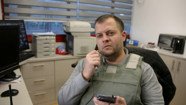 man in bulletproof vest in security room speaks phone