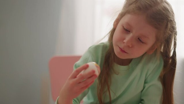 Thoughtful little girl holds Easter egg colored with marbling patterns in room closeup slow motion. Creative ideas for spring holiday decorations
