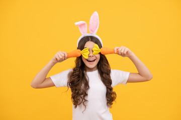 funny teen girl in bunny ears hold carrot on yellow background, easter