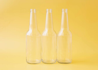Three empty glass beer bottles stand on a bright yellow background
