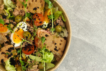 Healthy bowl with tuna, eggs, tomatoes, breads, lettuce, olives and greens in eco paper box isolated on gray background. Restaurant food delivery service and daily ration concept. Nicoise salad.