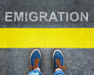 Women's feet in sneakers stand at the line with the inscription "emigration".	