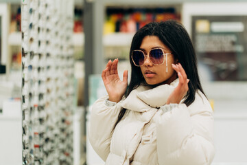 A young African American woman chooses glasses in an optics store.