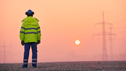 Rear view of electrical engineer against electricity pylons during frosty winter morning. Themes...