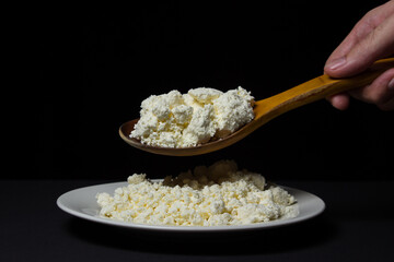 A plate of cottage cheese on a black background. Healthy and tasty dairy product. Wooden spoon full of cottage cheese