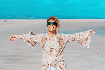 Happy standing pretty adult woman at the beach outstretching arms with tropical summer holiday beach and ocean in background. Concept o travel and wanderlust active female solo people lifestyle - obrazy, fototapety, plakaty