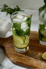 Non-alcoholic mojitos with ice, mint and lime slices on wooden board. Refreshing summer cocktails.