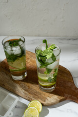 Non-alcoholic mojitos with ice, mint and lime slices on wooden board. Refreshing summer cocktails.