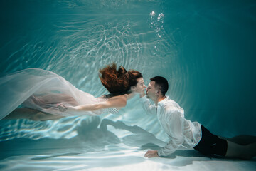 Romantic wedding pair is kissing underwater in pool with blue background. Young couple kissing underwater