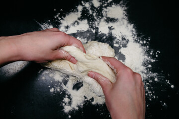 Pizza dough on a black table with hands
