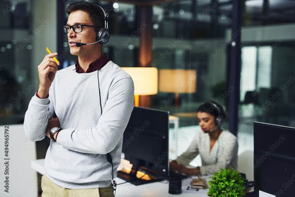 Poster Lets solve your problems one by one.... Shot of a young call centre agent working late in an office.