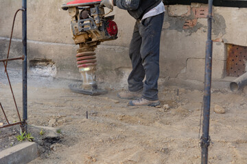 Worker uses a portable vibration rammer at construction a formwork for a blind area at home