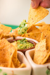 Vertical shot of a hand dipping nachos on a guacamole sauce