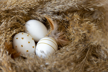In a nest made of dry material, chicken eggs lie as a symbol of the upcoming holiday - Easter. Eggs have an ornament in gold color 