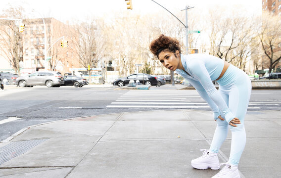 Mixed race woman wearing powder blue fitness clothes catches her breath during exercise outside on city sidewalk