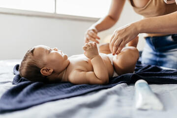 Mother changing baby's diaper in bed. Mother applies diaper rash cream. - obrazy, fototapety, plakaty