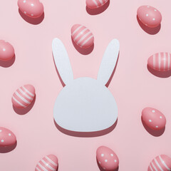 Easter bunny head shape surrounded with colored eggs on pastel pink background. Minimal Easter concept. Traditional spring holiday greeting card or banner with copy space for text. Flat lay.