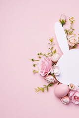 Easter bunny head shape surrounded with colored eggs and fresh flowers on pastel pink background. Minimal Easter concept. Traditional spring holiday greeting card or banner with copy space for text.	