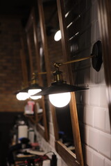 many copper lamp sconce hanging from white tile wall near big mirrors in beauty salon