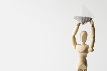 Mannequin holds a tea bag-pyramid with black tea flavored, with fruits and berries. Possible element of the interior of the kitchen, dining room or cafe. Copy space. Light background